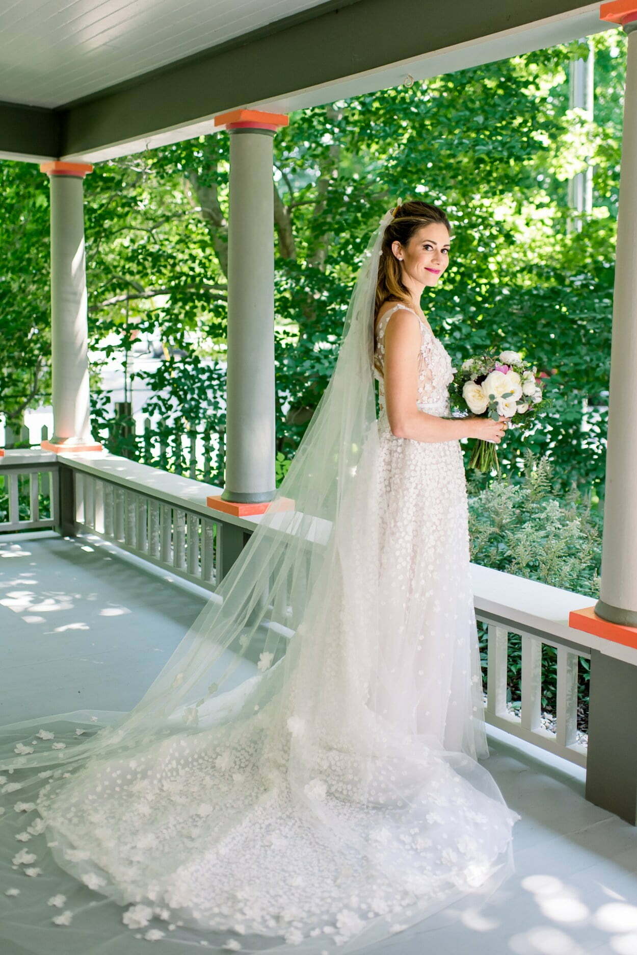 Smiling bride with bouquet on porch.