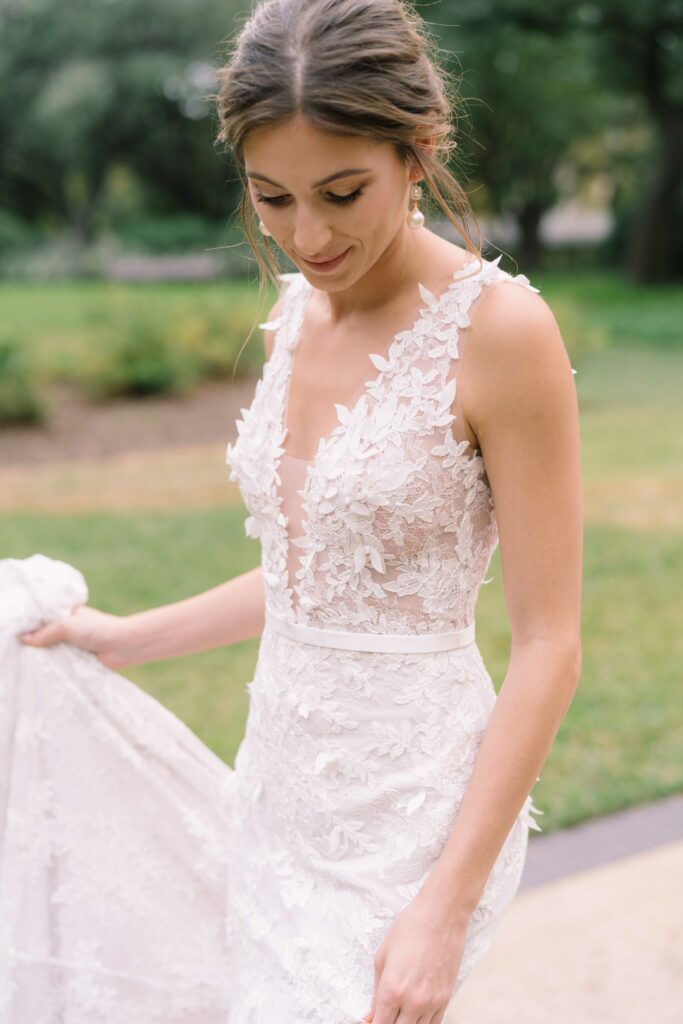 Bride in lace gown smiling on lawn.
