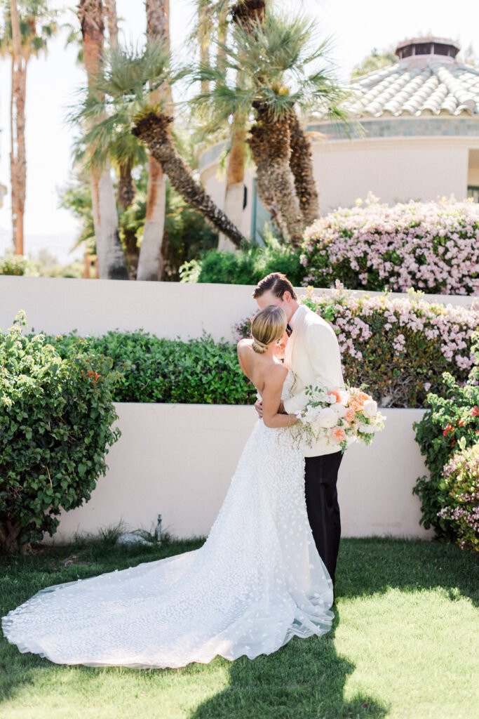 Bride and groom embrace amid flowers outdoors.