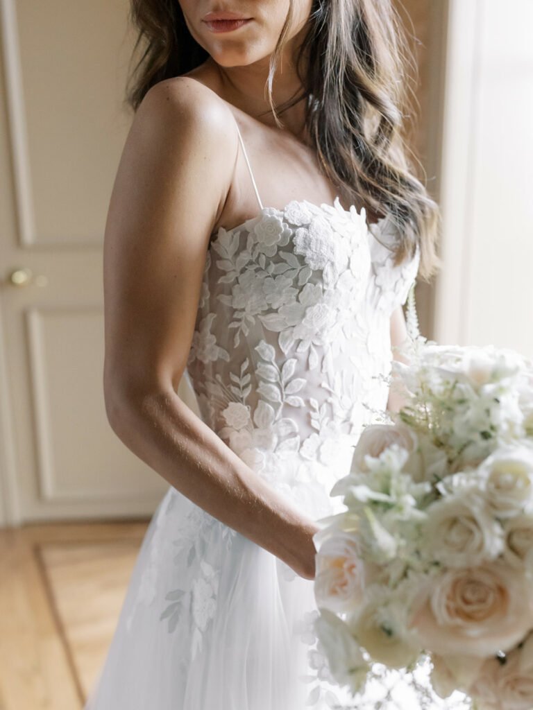 Bride in lace dress holding rose bouquet.