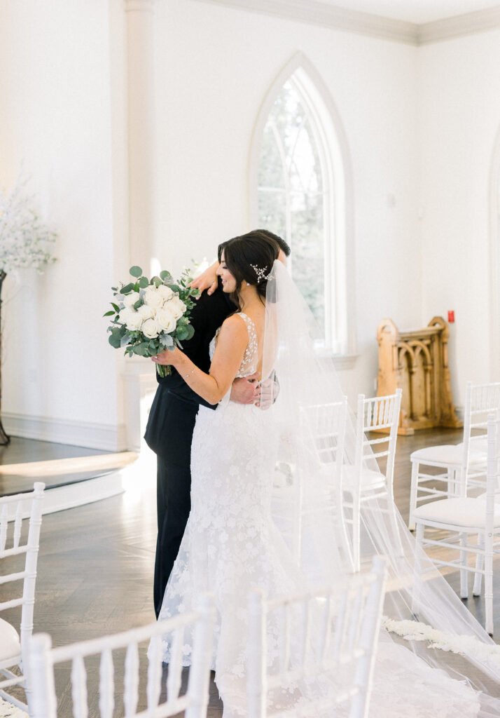 Bride and groom embrace in sunlit room.