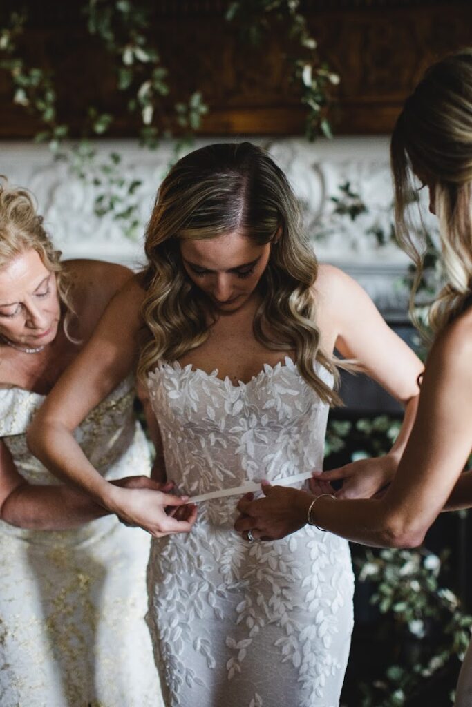 Bride assisted with sash by two women.