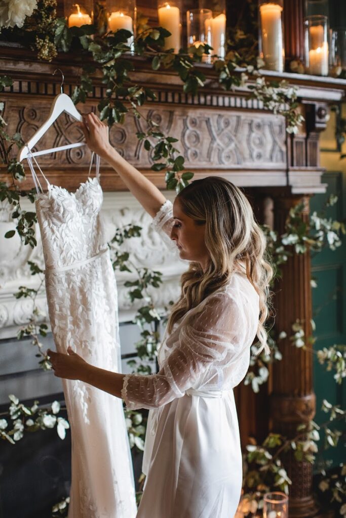 Woman holds lace wedding dress by mantle.