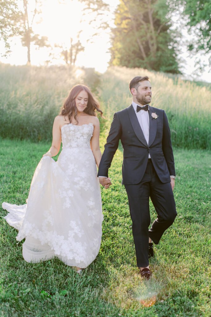 Bride and groom walk hand in hand outdoors.