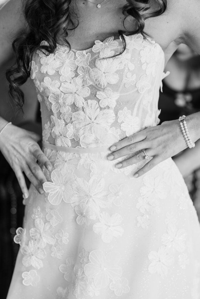 Bride in floral lace dress, hands on waist.
