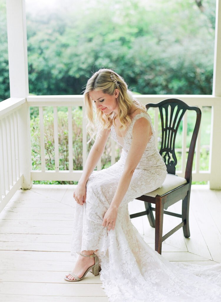Bride adjusts sandal on porch chair.