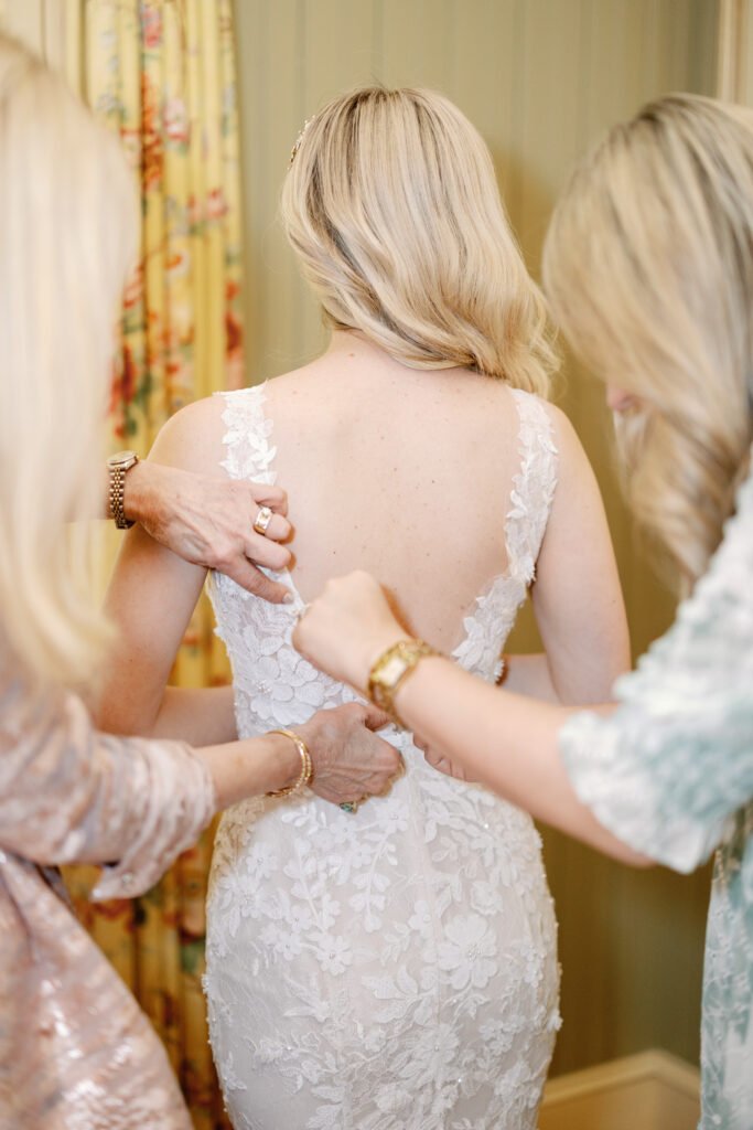 Bride in lace dress helped by two women.