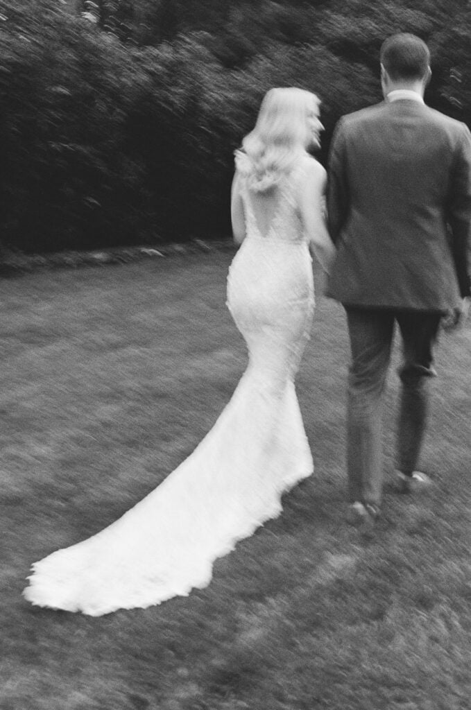 Bride and groom walking away on grass.