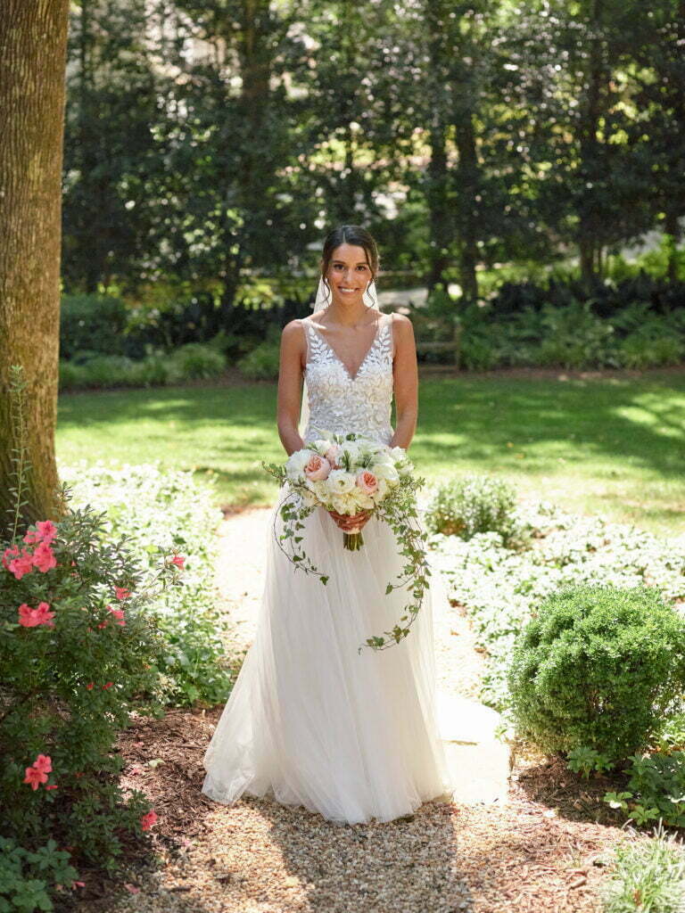 Bride with bouquet on sunny garden path.