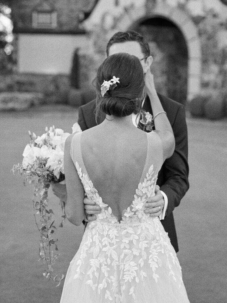 Bride and groom embrace outdoors by stone building.