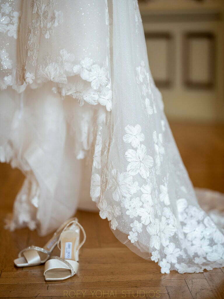 Wedding dress and ivory heels on wooden floor.