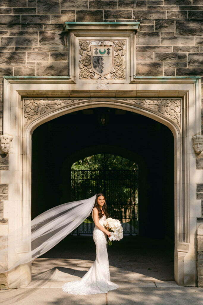 Bride in white under stone archway, sunlight shining.