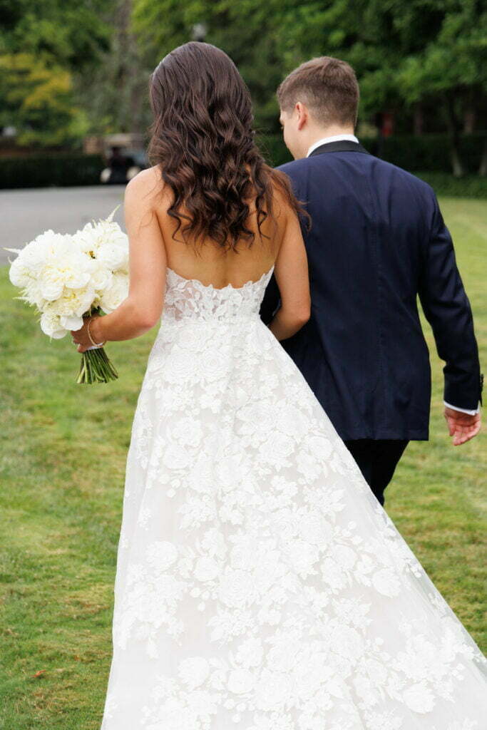 Bride and groom walking away on grassy path.