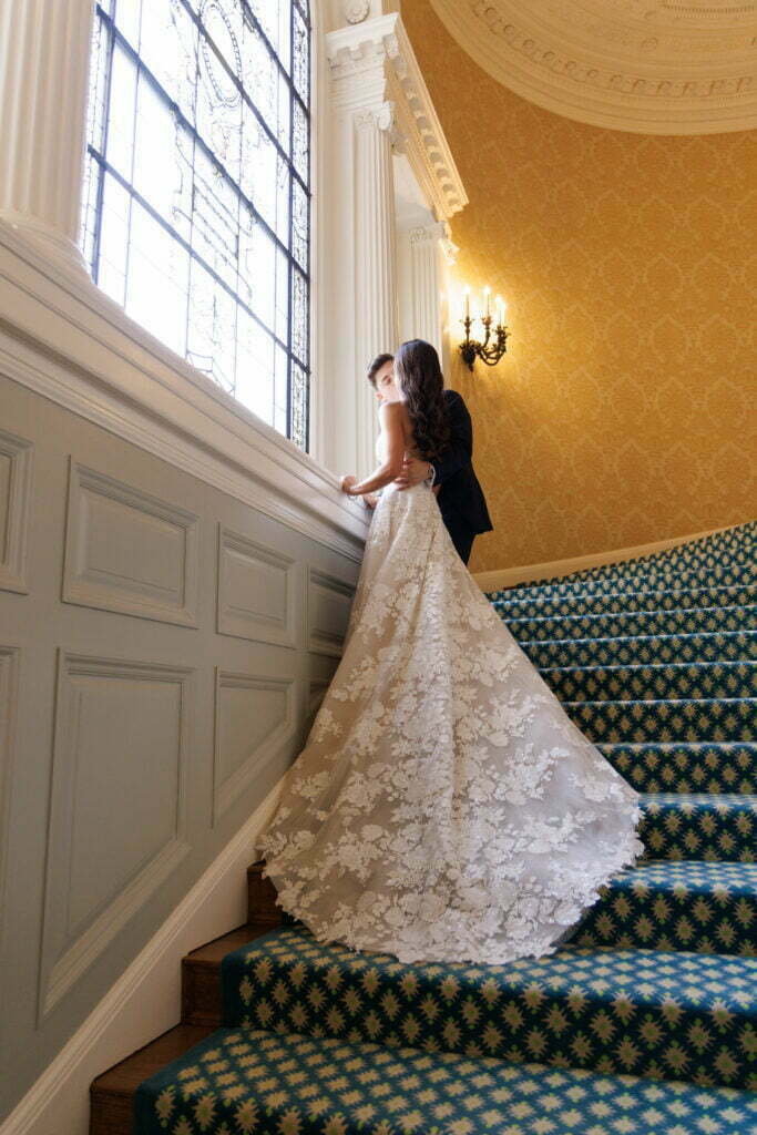 Bride and groom on staircase by large window.