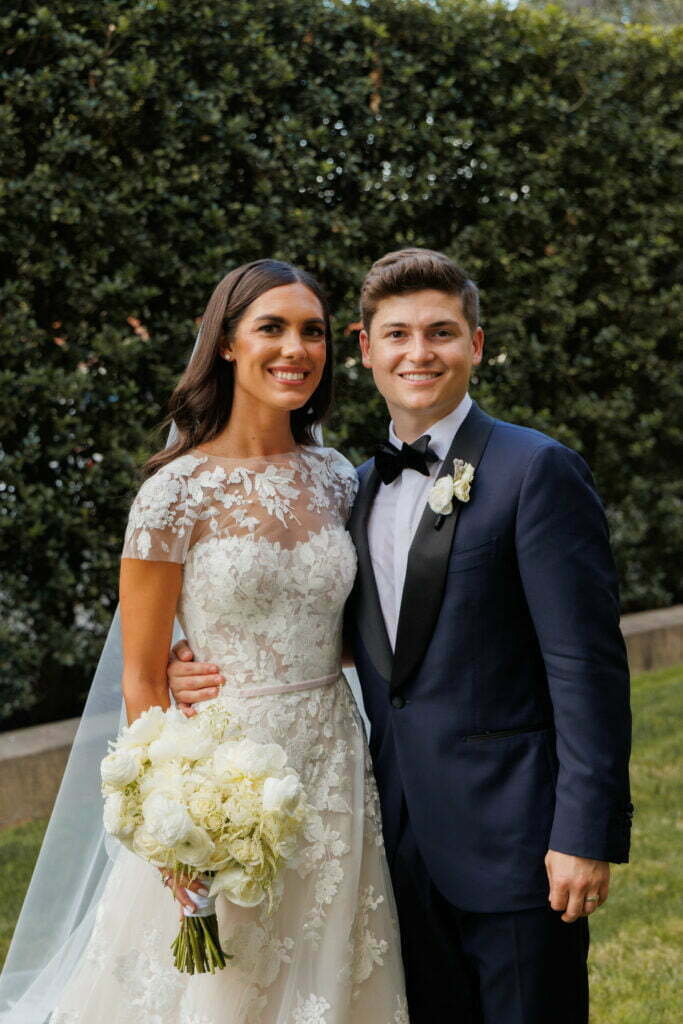 Smiling bride and groom outdoors with bouquet.