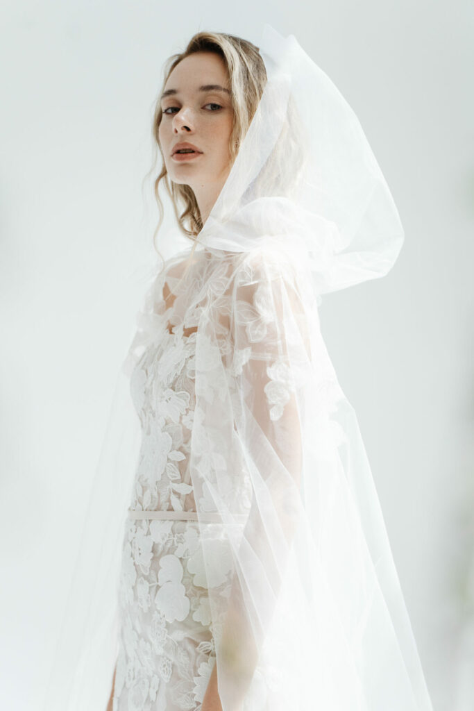 Bride in lace dress and veil, confident pose.