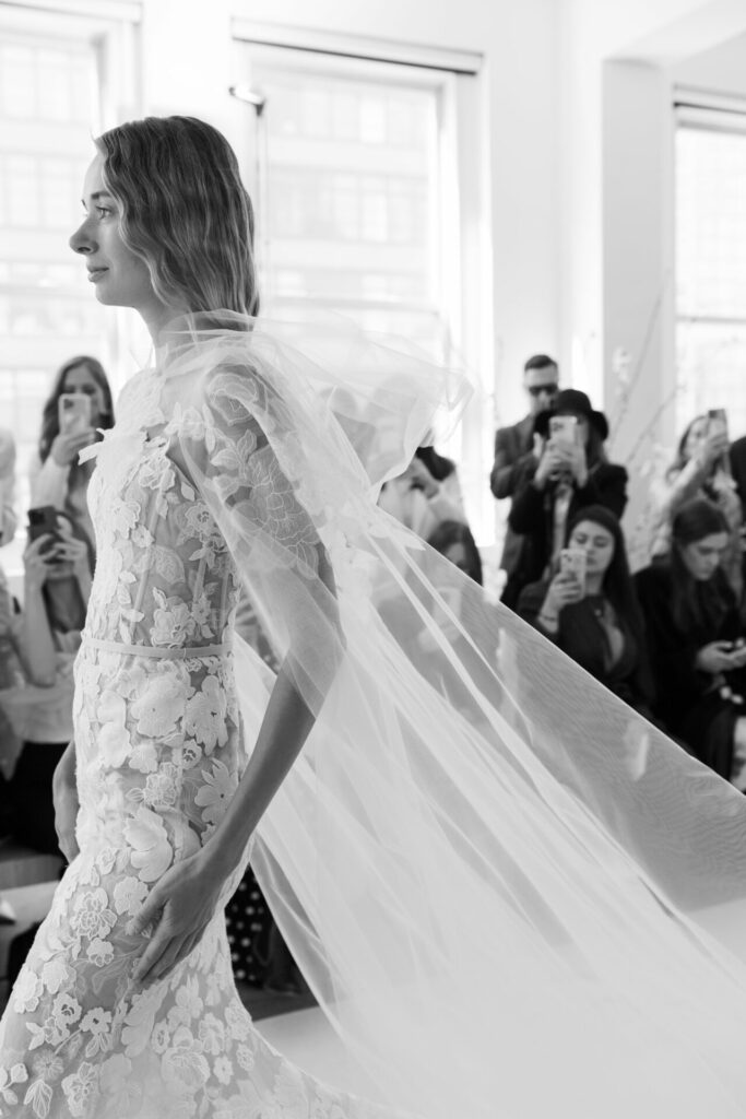 Bride with veil walks past crowd, black-and-white.