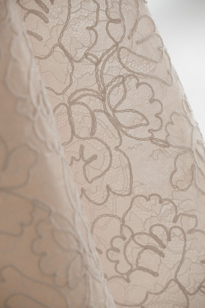 Sheer beige lace fabric with floral embroidery.