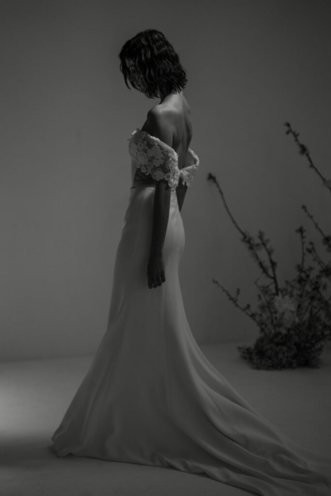 Bride in lace dress, soft light, floral backdrop.