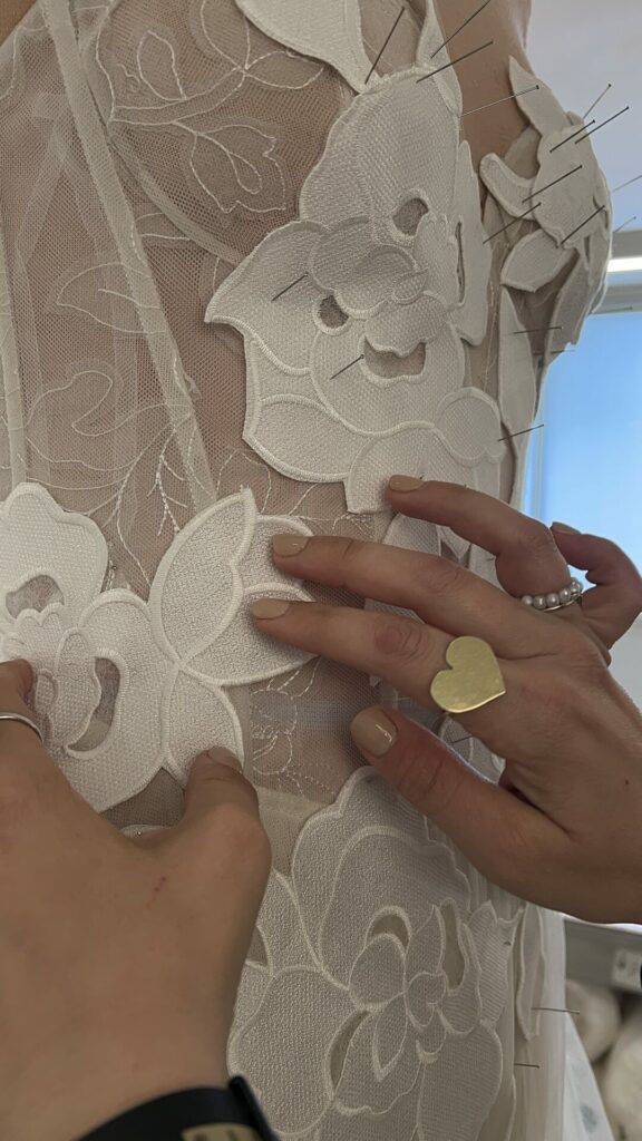 Hands adjust lace on sheer dress, rings visible.