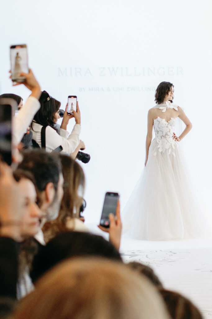Model in white floral gown on runway.