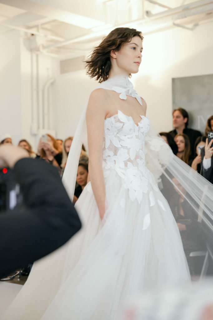 Model in white floral gown on runway.