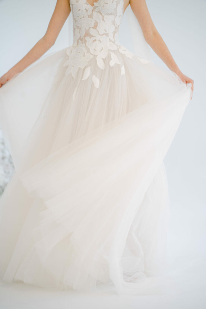 Person in white wedding dress holding skirt out.