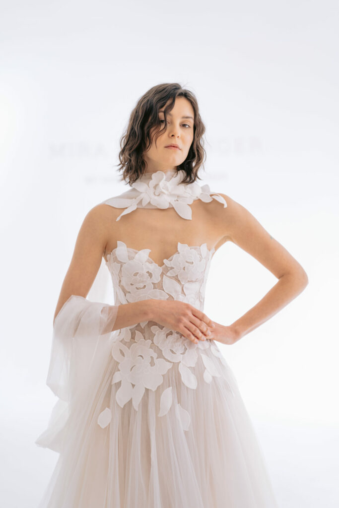Woman in floral wedding dress poses confidently.