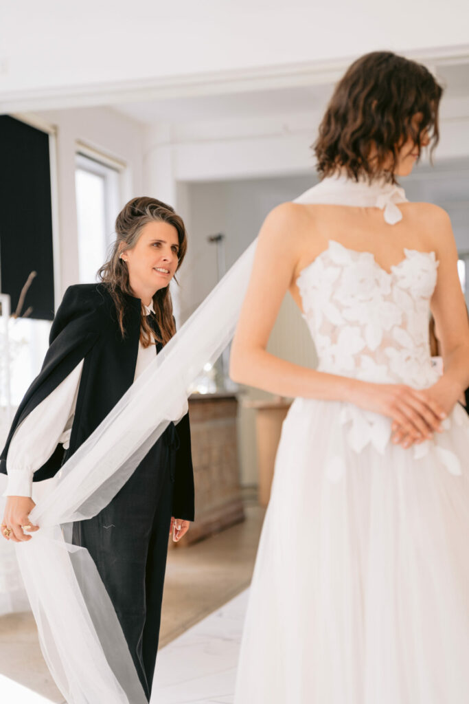 Woman adjusts train of bridal gown indoors.