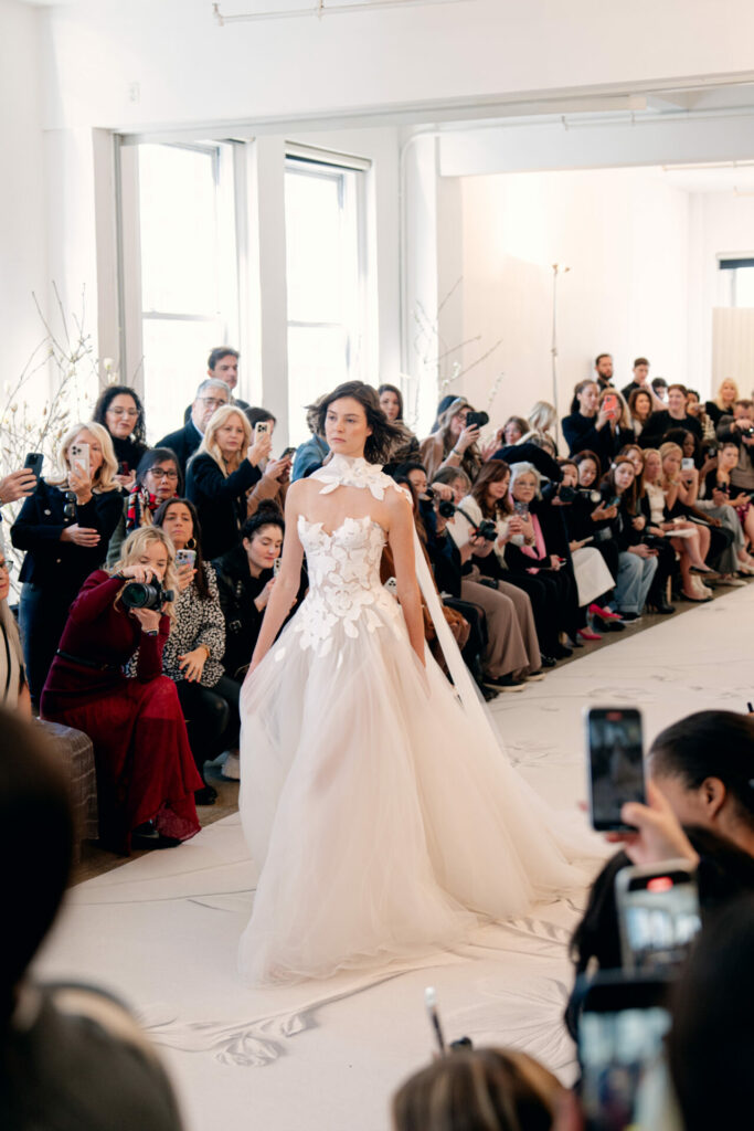Model in floral wedding gown on runway.