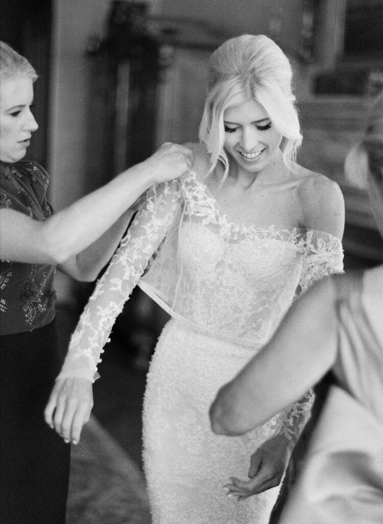 Bride in lace gown, smiling with friends.