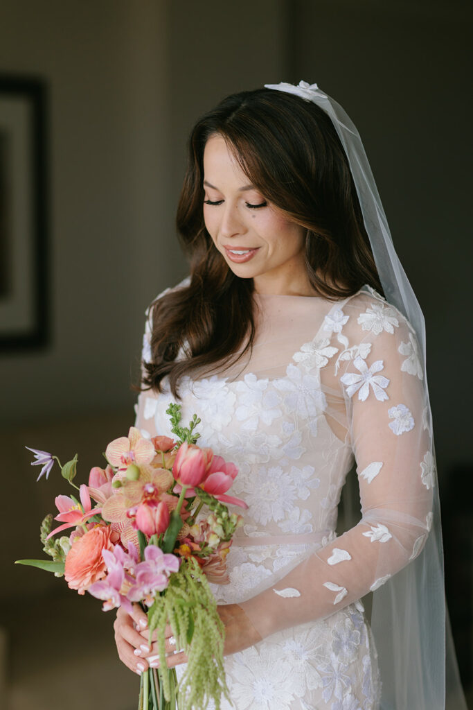 Bride in lace dress smiles, holding bouquet.