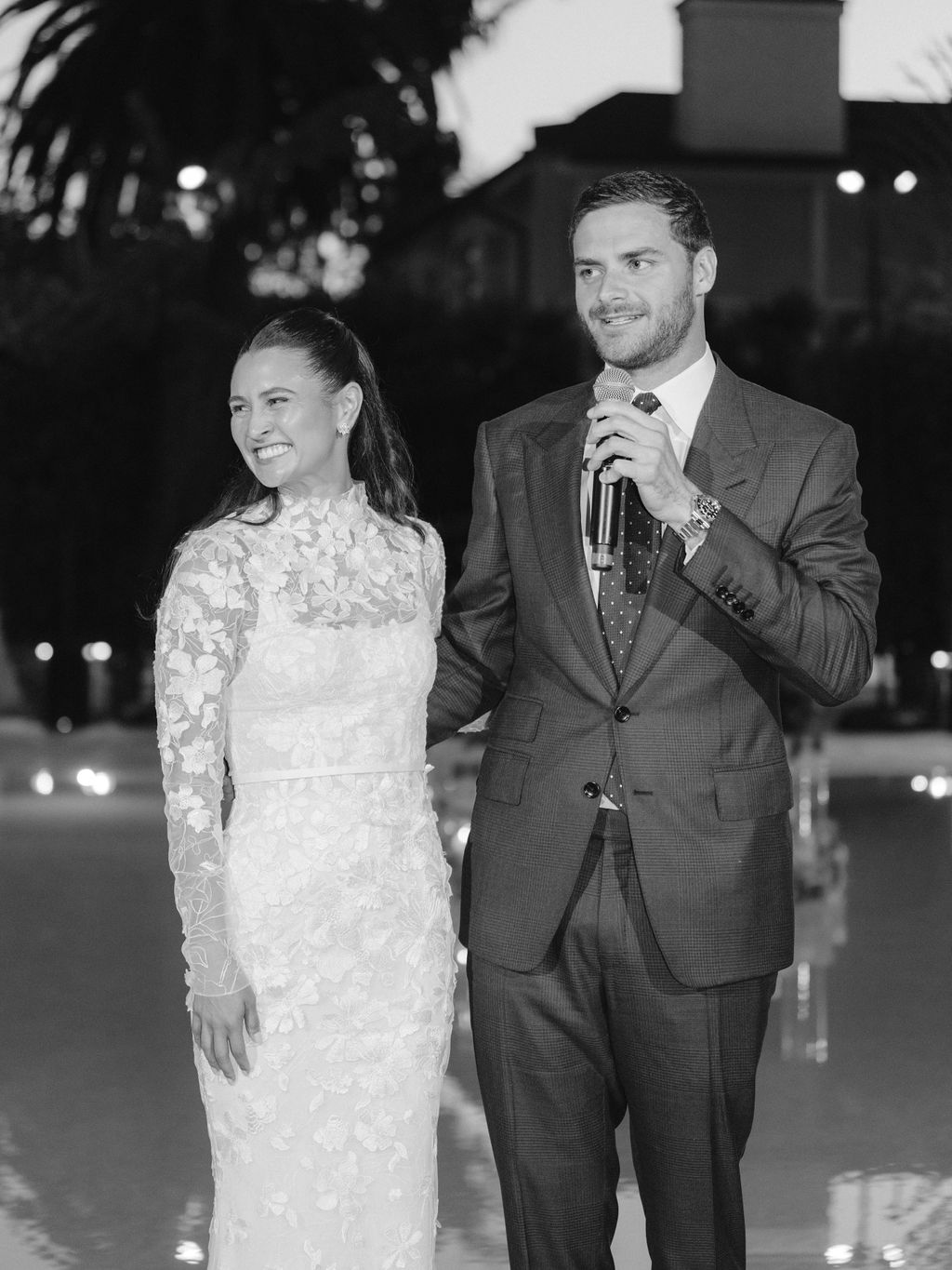 Bride in lace dress smiles, man speaks.