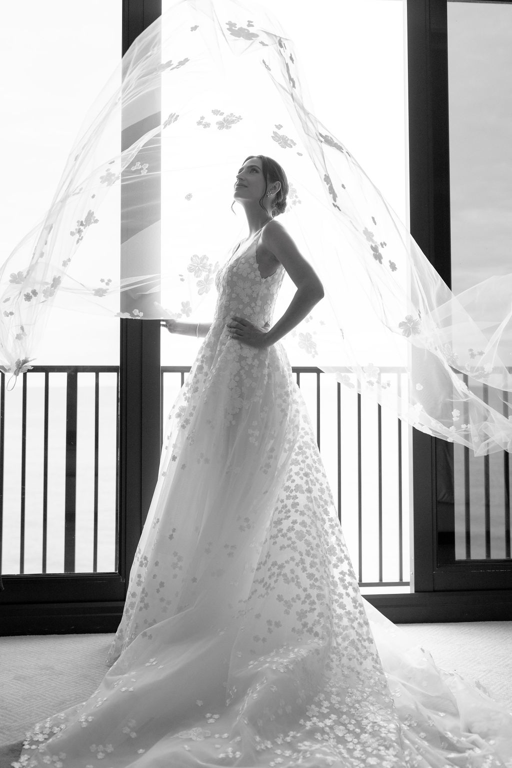 Bride in floral dress, veil lifted, backlit.