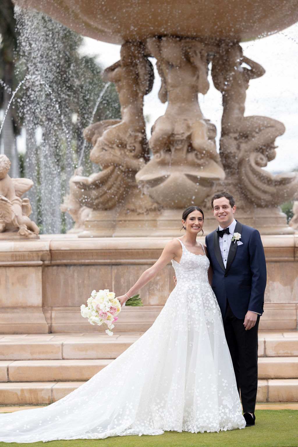 Smiling bride and groom by ornate fountain.