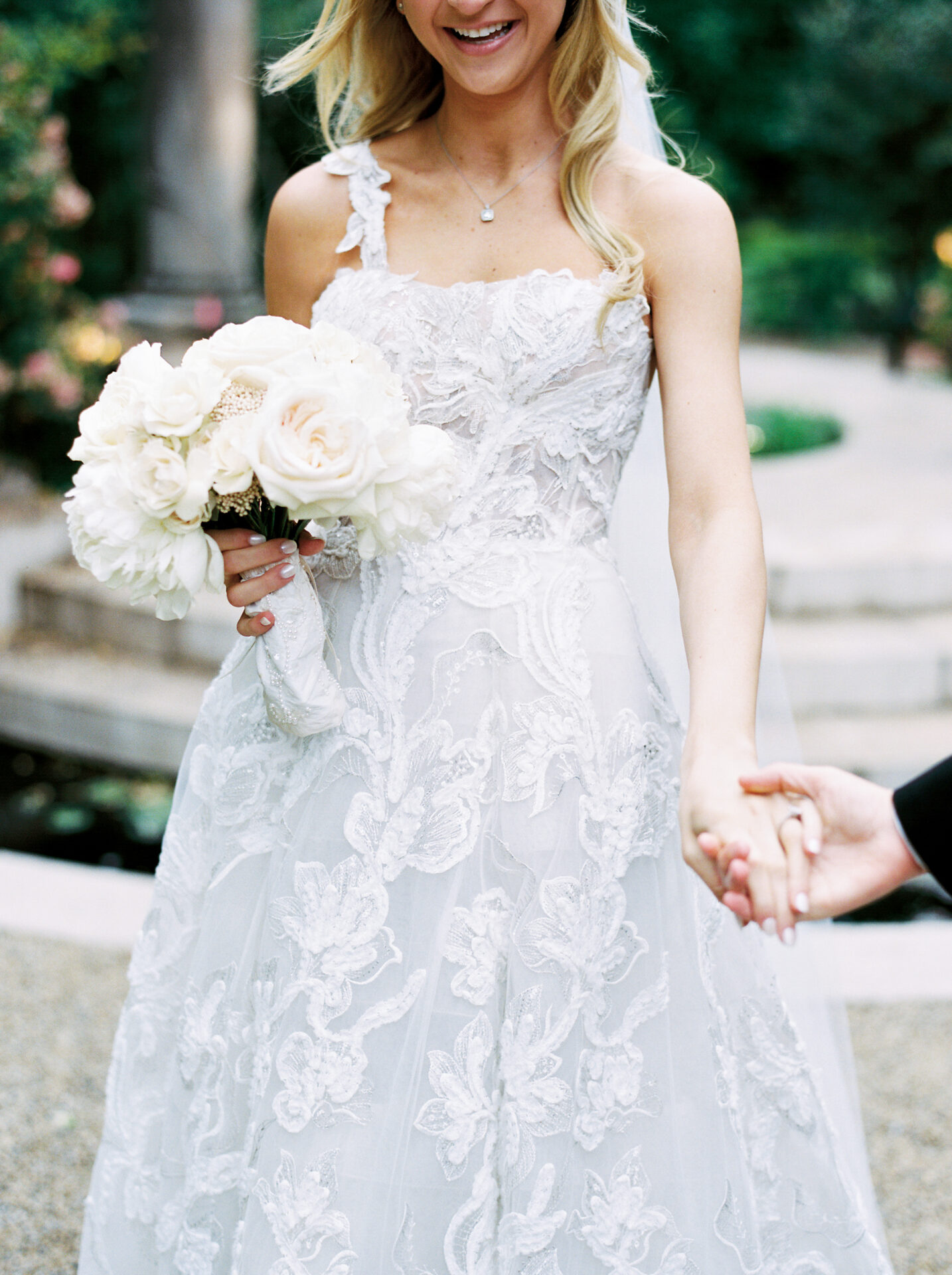 Bride in lace dress smiles, holding bouquet.