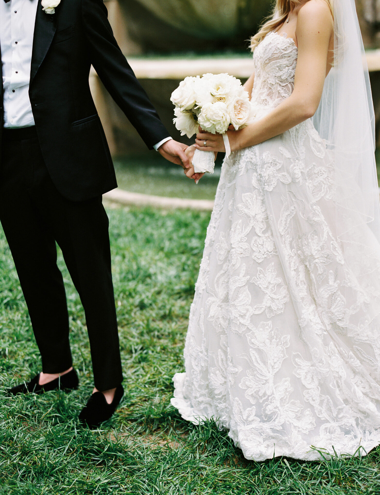 Bride and groom holding hands on grass.