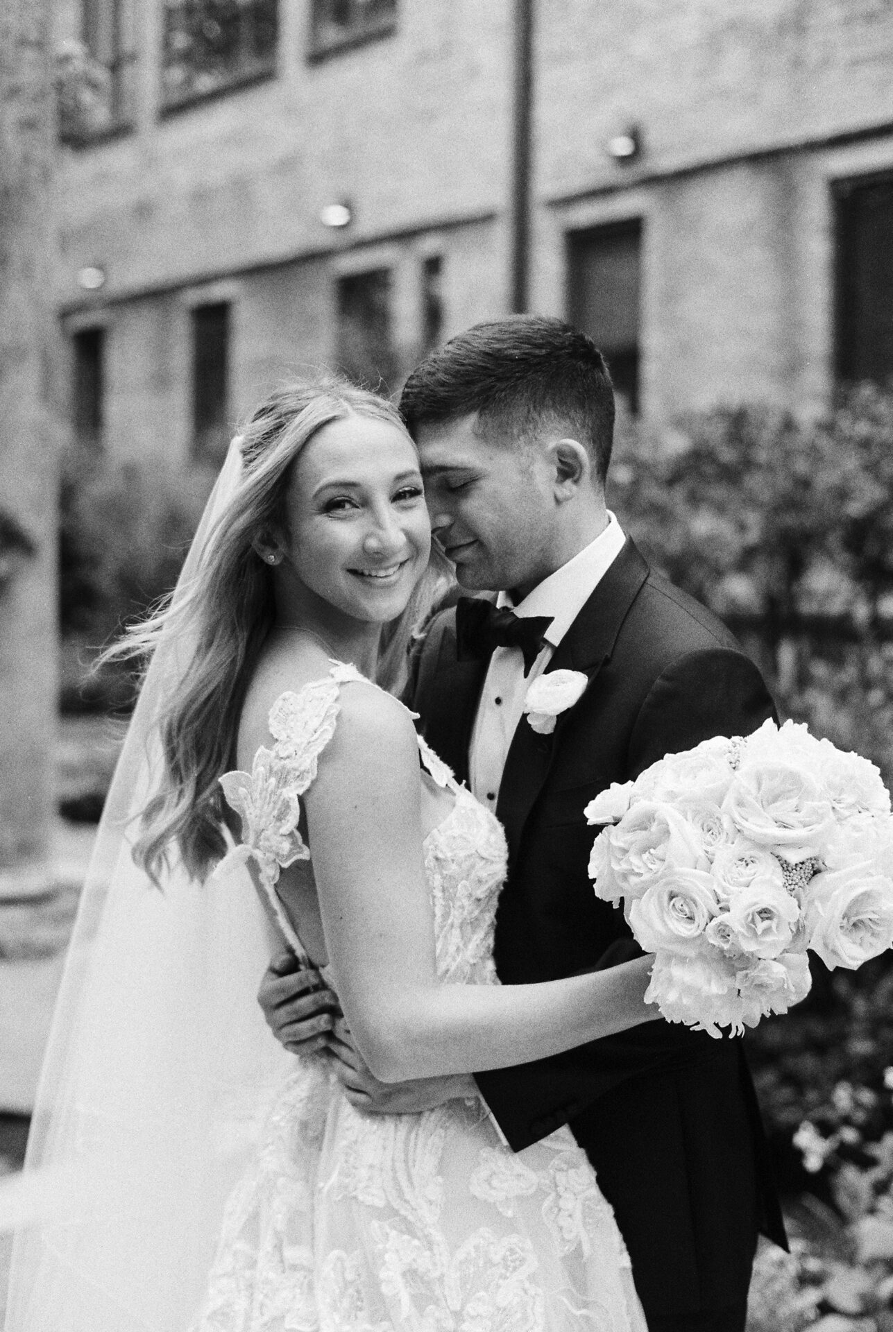 Bride and groom smiling, embracing outdoors.