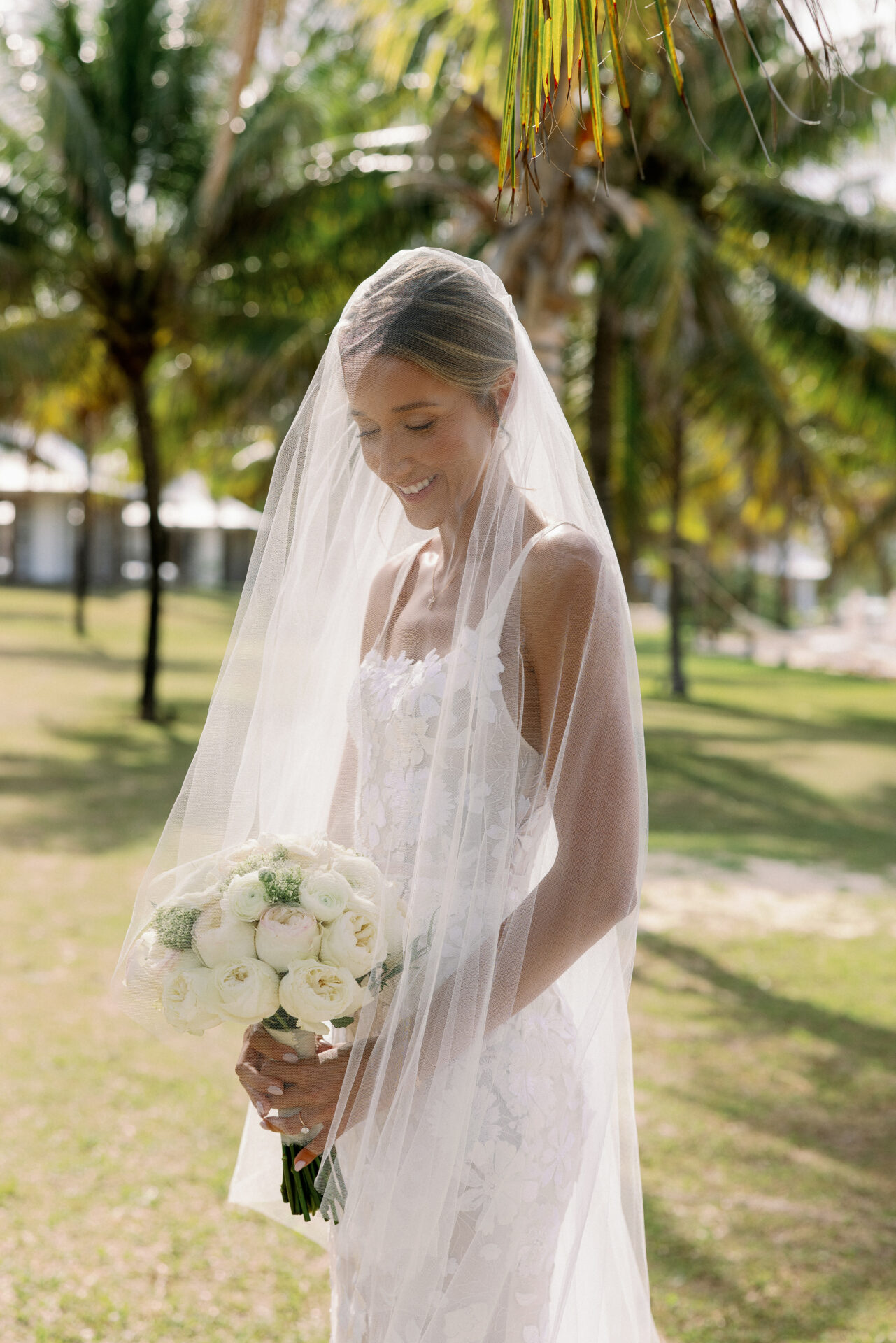 Bride holding bouquet under palm trees.