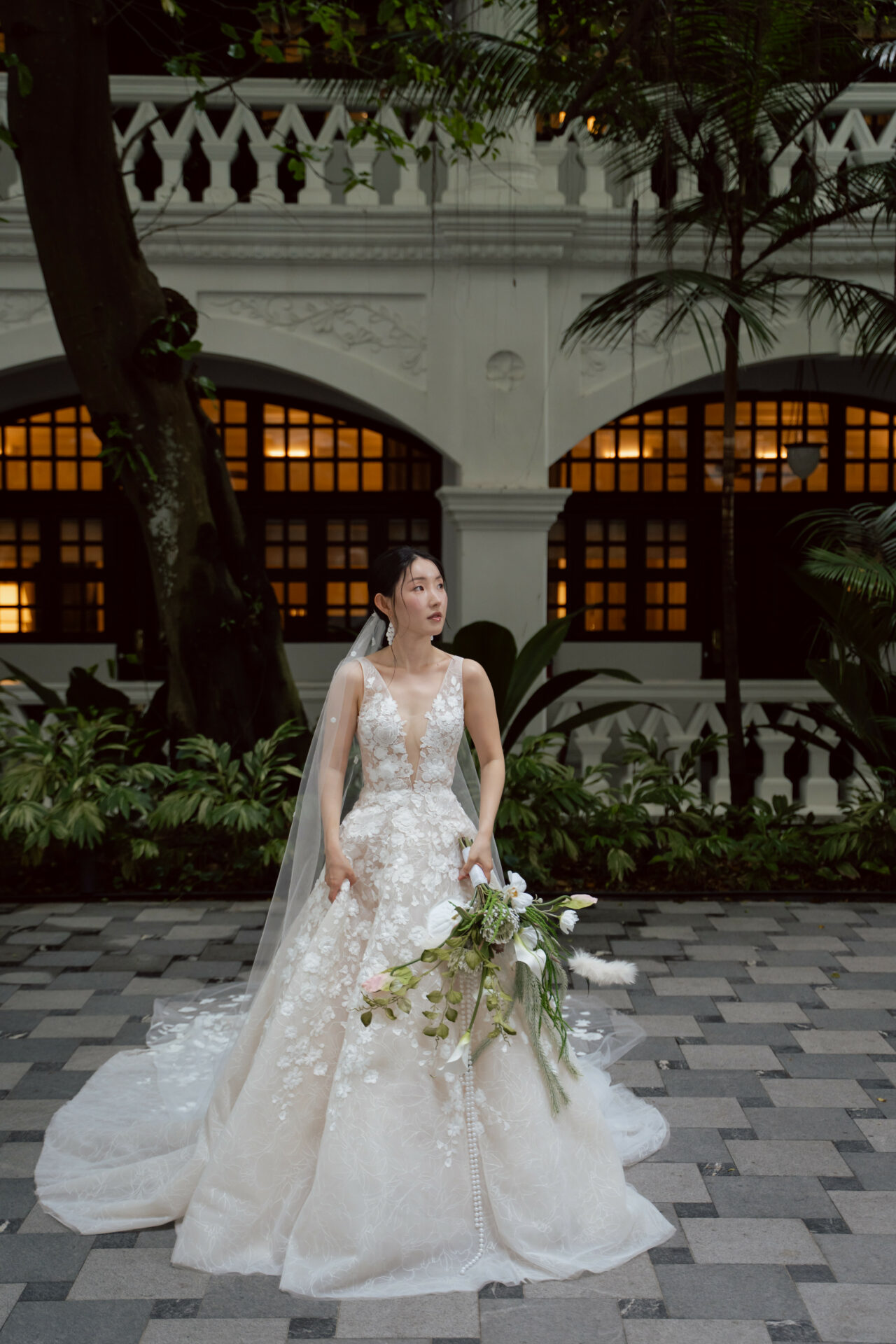 Bride in lace gown holding white bouquet outdoors.