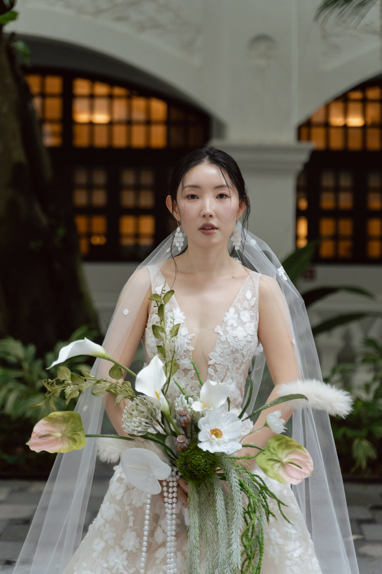 Bride in lace gown holding bouquet indoors.