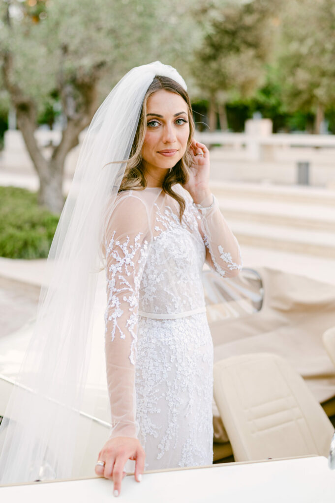 Bride in lace gown by convertible outdoors.