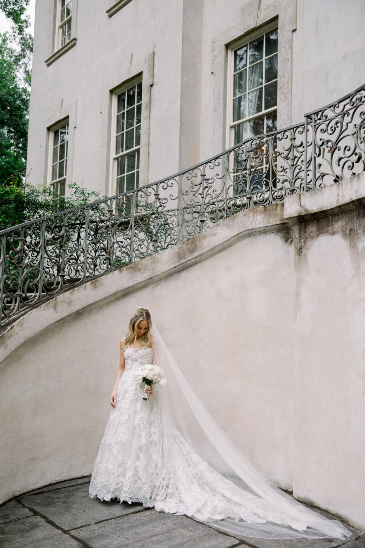Bride in lace dress by railing and building.