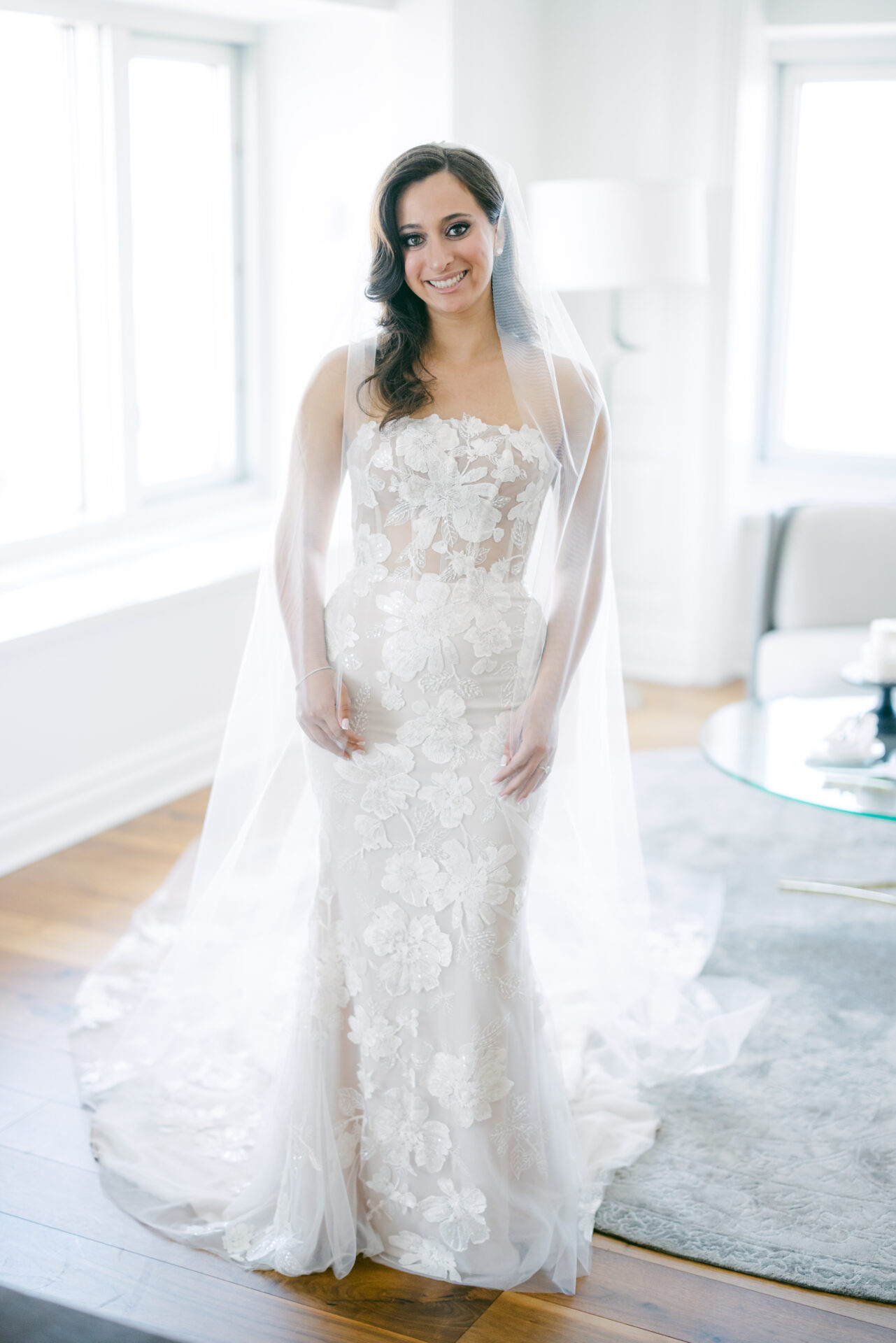 Smiling bride in lace dress by sunny windows.