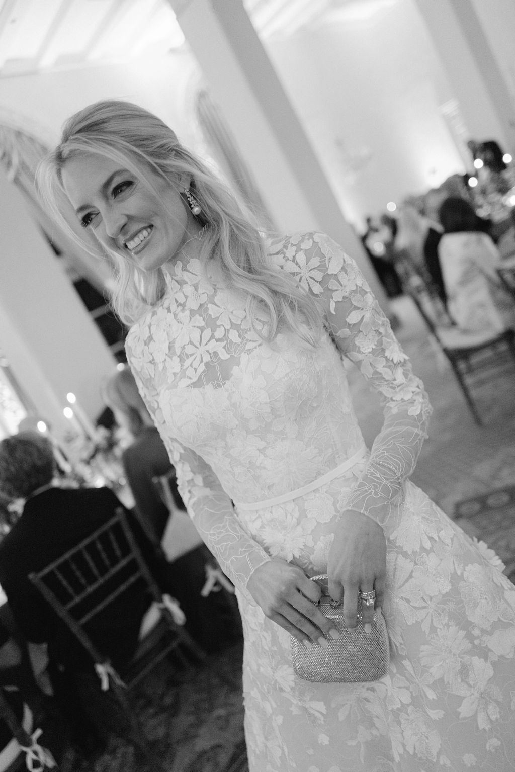 Smiling bride holds clutch at indoor event.