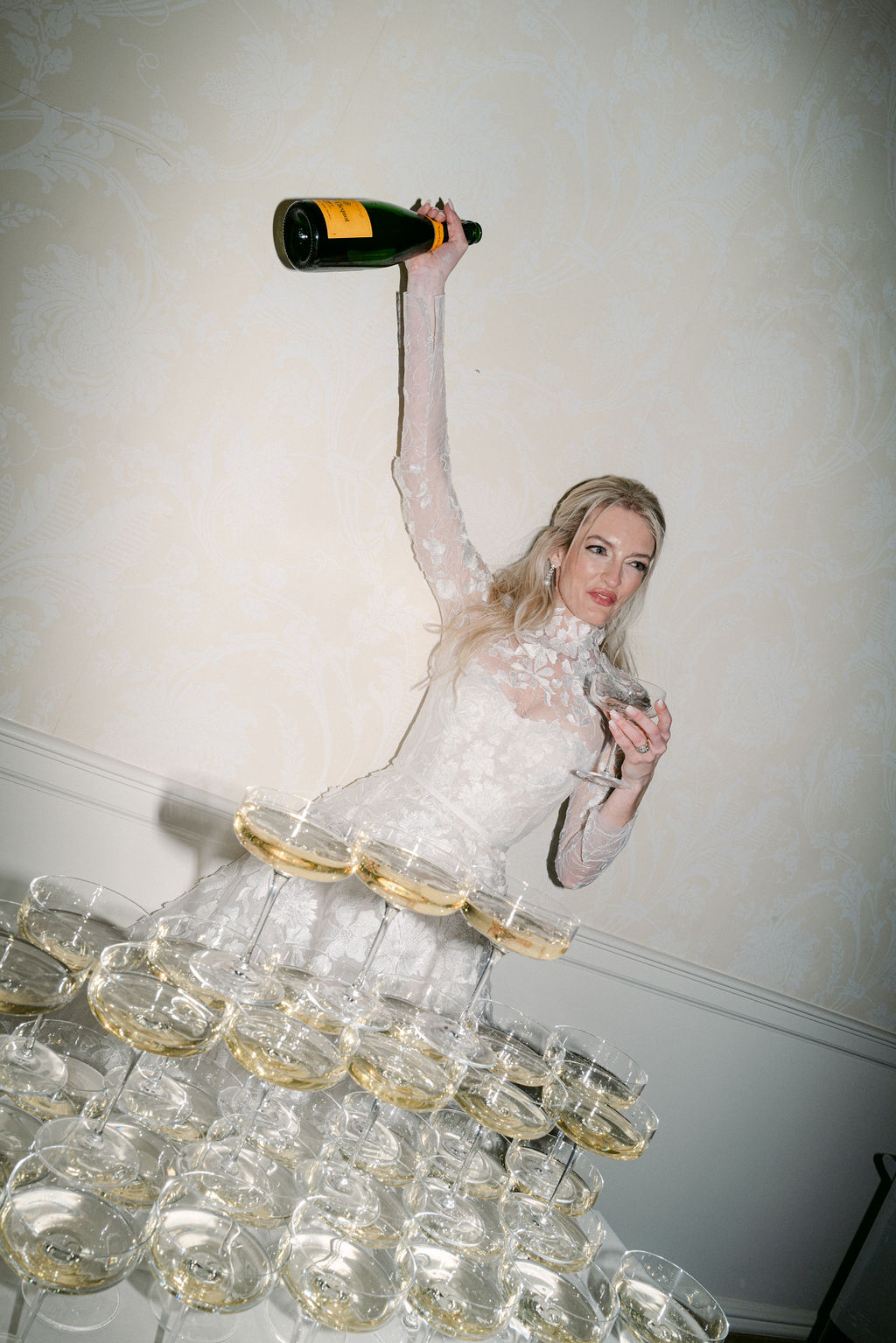 Woman pours champagne into glass pyramid, posing.