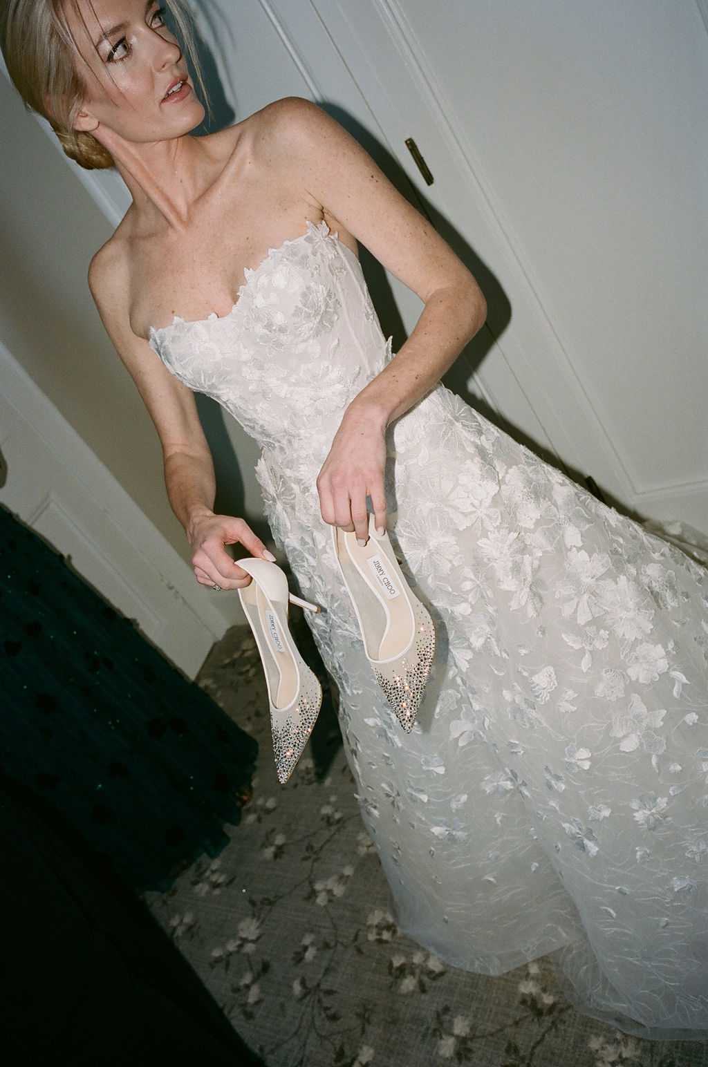 Woman in floral gown holding sparkly heels.