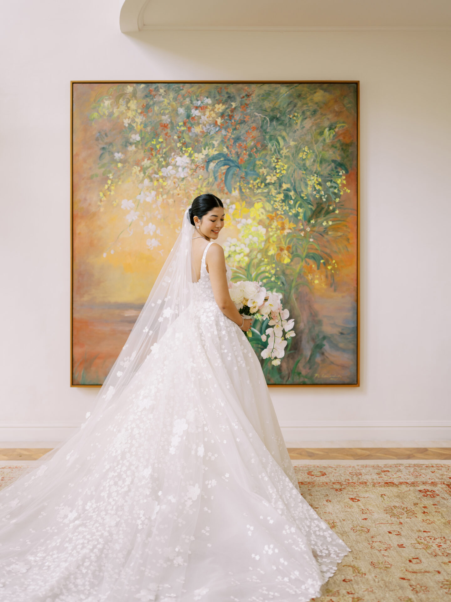 Bride in floral gown smiles by flower painting.
