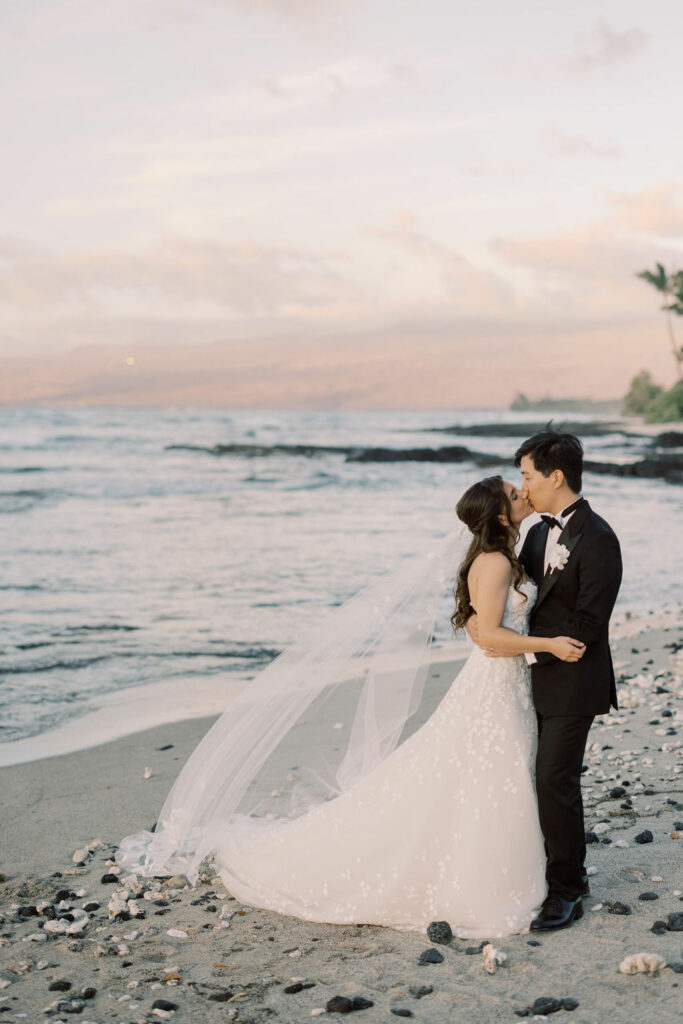 Bride and groom kiss on sunset beach.