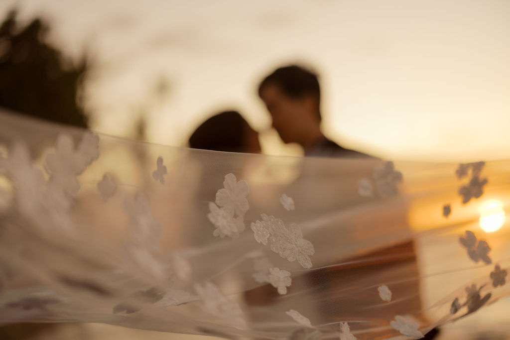 Sheer floral veil blows over blurred couple.
